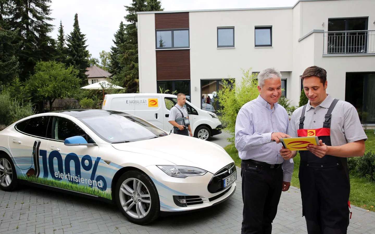 E-Mobilität - Mitarbeiter mit Kunden vor Elektrofahrzeugen 100% elektrisch &middot; Elektro-Stock