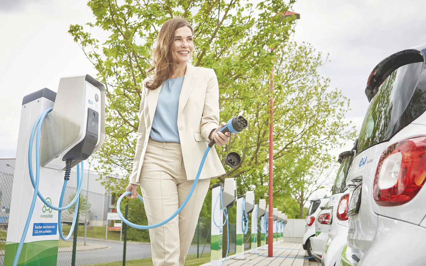 E-Mobilität - Kundin vor Ladestation mit Stecker in der Hand &middot; Elektro-Stock